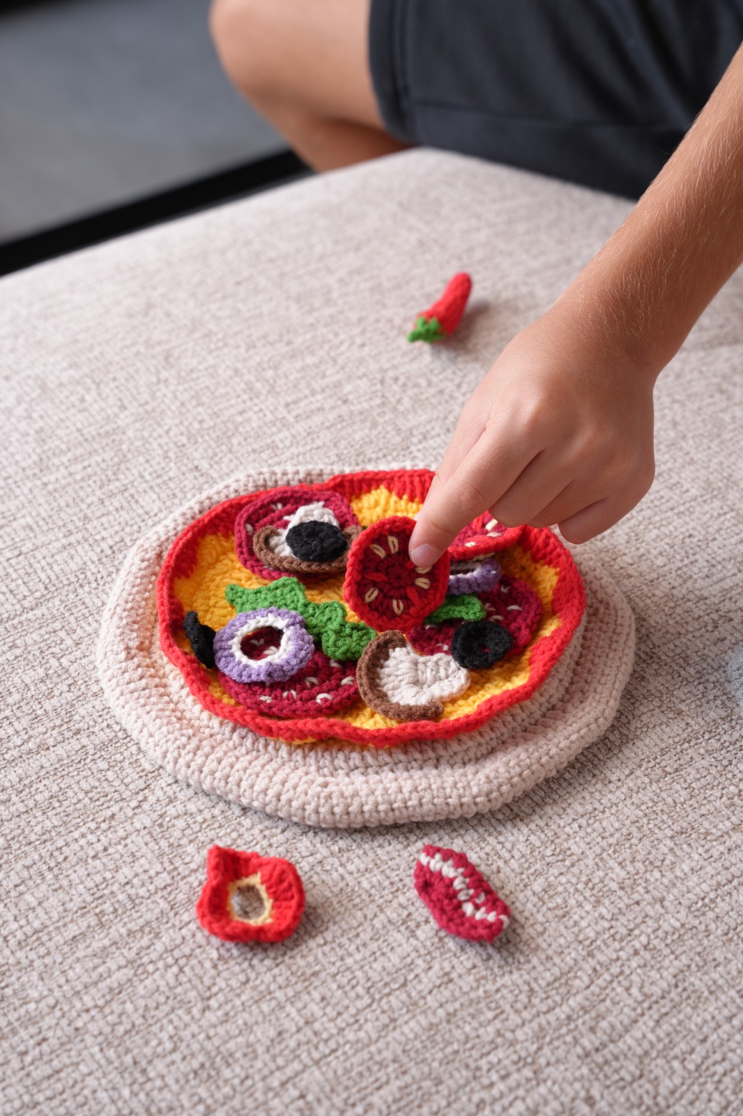 Child placing crochet toppings on the Little Pizzeria pizza